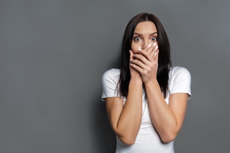 a woman in a white shirt covering her mouth with a shocked expression